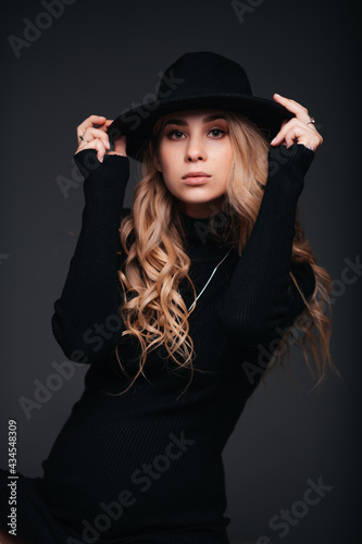 Portrait of a young beautiful woman in black hat on black background © Илья Солдаткин