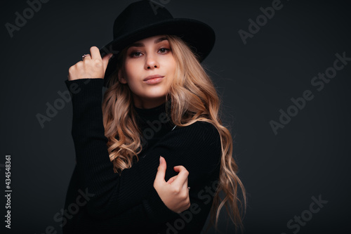 Portrait of a young beautiful woman in black hat on black background © Илья Солдаткин