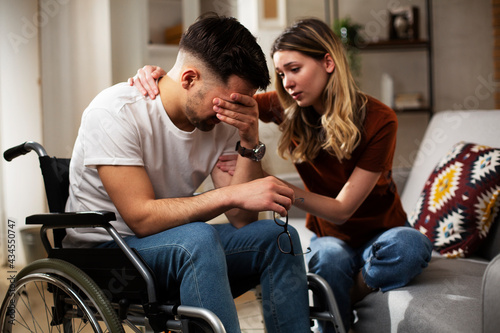 Young man in a wheelchair. Girlfriend comforting her sad boyfriend...
