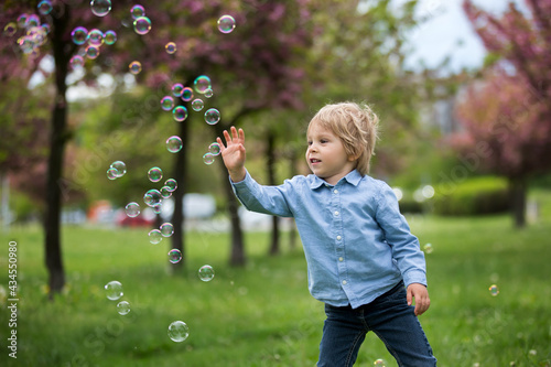 Blond toddler child, cute boy in casual clothing, playing with soap bubbles in the park