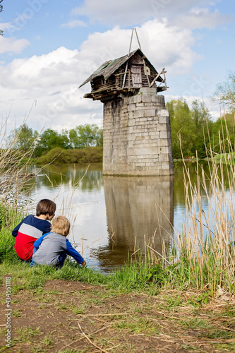 Children, playing on the river in front of old wooden cottage on brick pillar, small cabin in Radbuza River, near Chotesov in Czech Republic photo