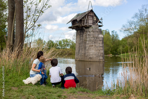 Family with children, feeding ducks in a river in front of old wooden cottage on brick pillar in The Radbuza River, near Chotesov, Czech Republic photo