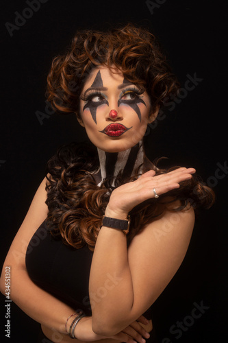 Woman with brown hair and painted face. Joker makeup. Pursed lips. Closeup of face