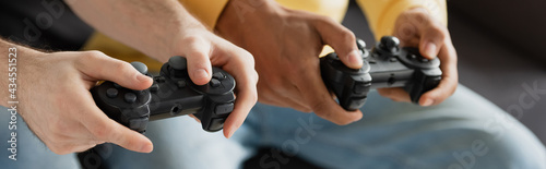 KYIV, UKRAINE - MARCH 22, 2021: cropped view of joysticks in hands of interracial men, banner