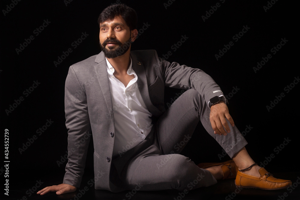Portrait of stylish man with black beard in formal grey suit without tie. Seated on floor looking up. Portrait of stylish man with black beard in formal grey suit without tie. Seated on floor looking up.