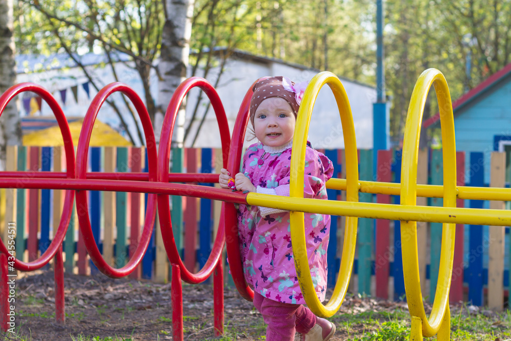 A little beautiful girl in a pink jacket does sports on the sports field in the spring