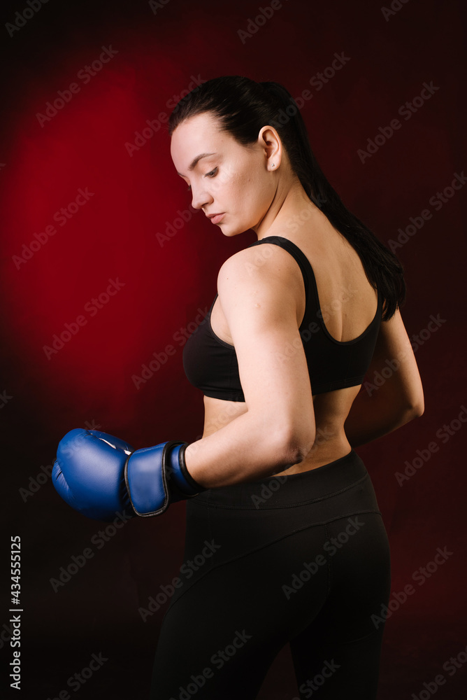 Strong sport woman boxer wearing blue boxing gloves on dark red background