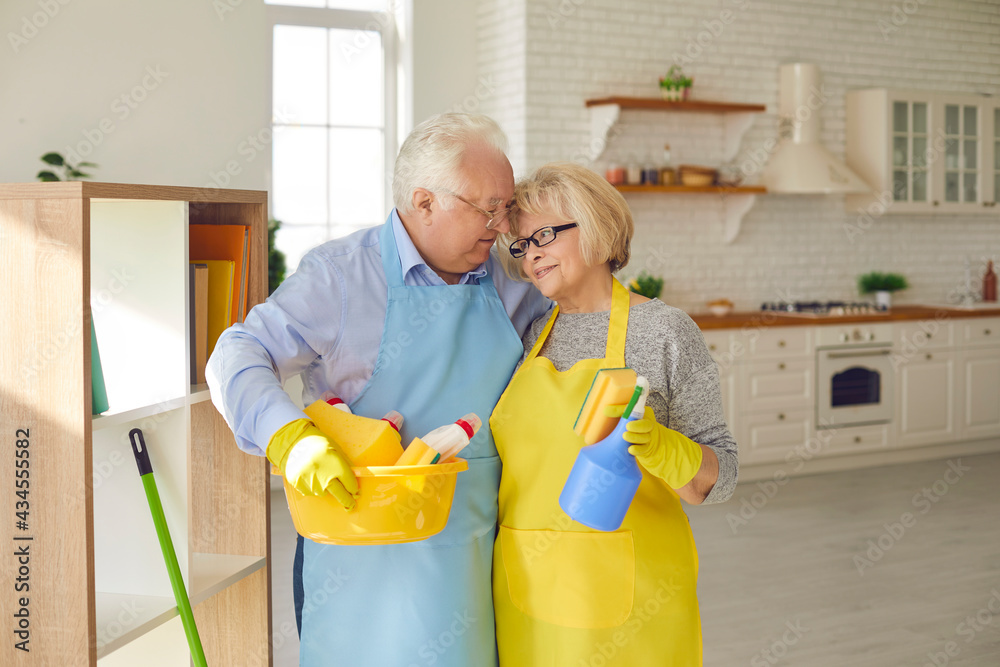 Φωτογραφία Loving mature couple in aprons and gloves holding equipment for home cleaning, hugging and feeling happy over spacious kitchen interior