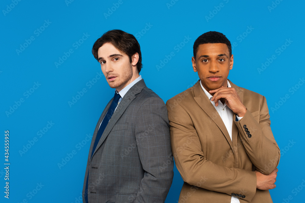 Elegant interracial men in suits standing together isolated on blue Elegant interracial men in suits standing together isolated on blue