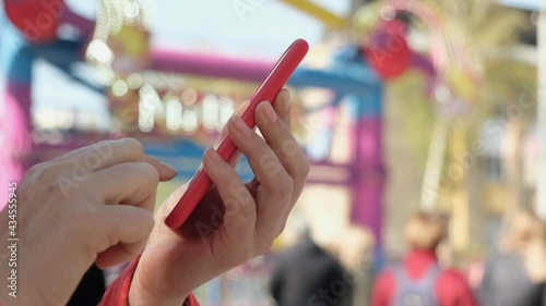 View of female hand holding and pressing on smartphone in the amusement park.