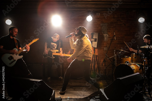 WIDE Punk rock band playing music during their concert on a stage of small venue. Vocals, guitars and drums. Shot with 2x anamorphic lens