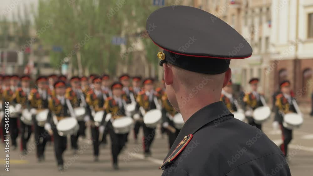 Close-up of a police officer watching soldiers marching in a military parade.