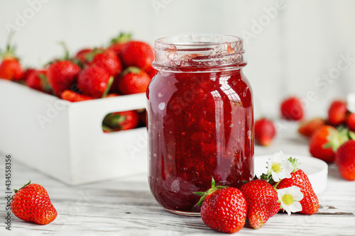 Homemade strawberry preserves or jam in a mason jar surrounded by fresh organic strawberries. Selective focus with blurred foreground and background. photo