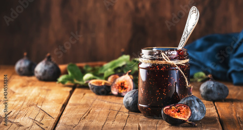 Red fig jam in jar with fresh blue figs. Homemade preparations and canning. Rustic wooden table background