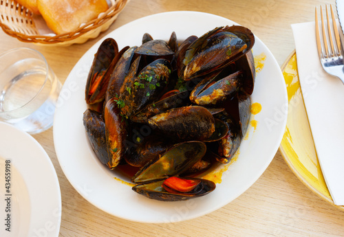 Delicious boiled mussels with tomato sauce and parsley in copper cooking dish