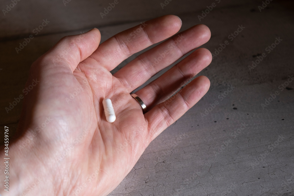 Male hand holding a white pill