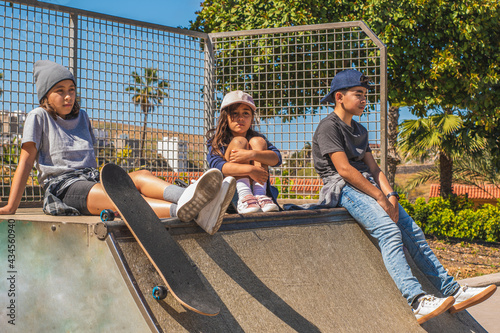 Three young skaters sitting on an obstacle on the skate park, hanging out or resting, with serious faces.