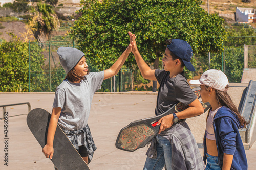 Three young skaters greet each other smiling in a skate park.