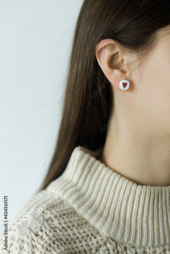 Beautiful stylish woman with cute earring with red heart, cropped view. Fashionable female in sweater with unusual fused glass accessory. Beauty and care. Valentine gift Beautiful stylish woman with cute earring with red heart, cropped view. Fashionable female in sweater with unusual fused glass accessory. Beauty and care. Valentine gift