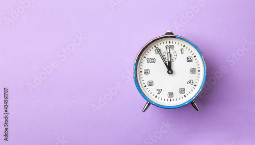 Old retro analog alarm clock in blue on a purple background. The clock starts from five minutes to twelve o'clock. Copy space.