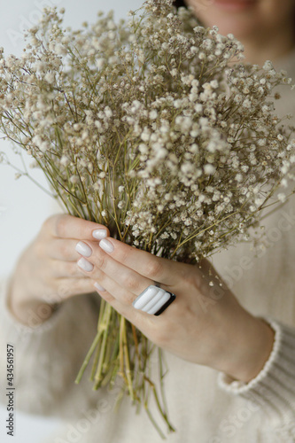 Beautiful stylish woman with modern square ring holding dried flowers. Fashionable female in sweater with unusual fused glass accessories and white manicure. Beauty and care concept