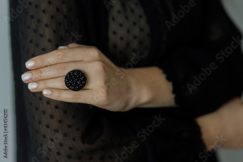 Beautiful stylish woman with modern round black ring on hand and white manicure, closeup. Fashionable female in black dress with unusual fused glass accessory. Beauty and care.