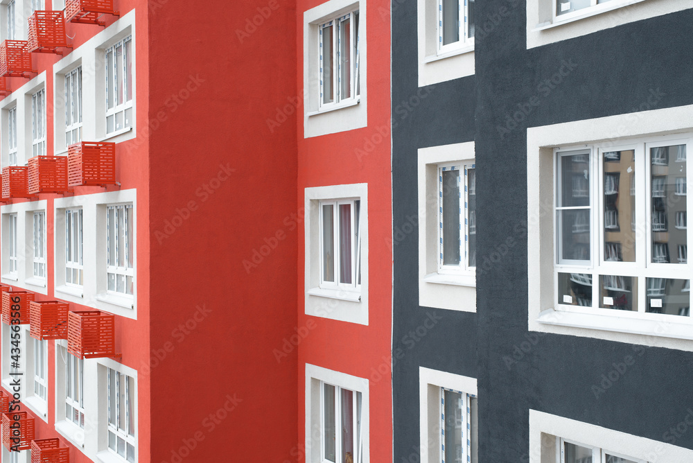 Facade of a multi-storey apartment building, exterior close-up. Multi-colored wall decoration and plastic windows outside.