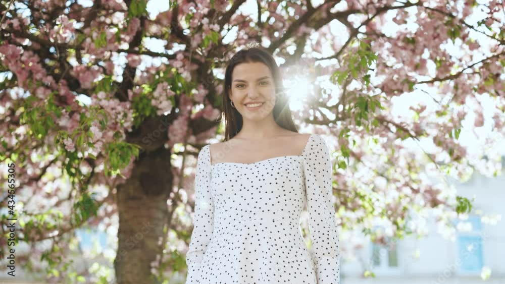 Portrait attractive sunshine young smiling woman with long hair look at camera smile portrait happy summer face sunset beautiful lady outdoor. Spring blossom of sakura tree in city park Portrait attractive sunshine young smiling woman with long hair look at camera smile portrait happy summer face sunset beautiful lady outdoor. Spring blossom of sakura tree in city park