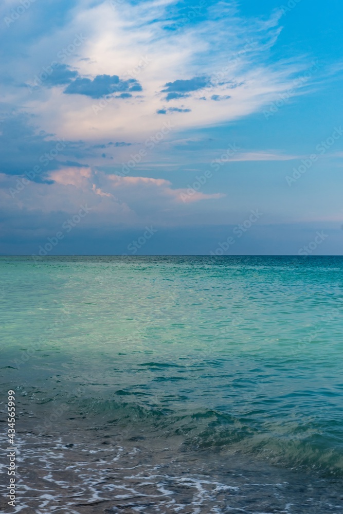 Beautiful seascape, green and turquoise tones and shades on flat sea water surface, blue sky, grey pink clouds before storm at sunset evening time. Natural colorful pattern background, vertical frame. Beautiful seascape, green and turquoise tones and shades on flat sea water surface, blue sky, grey pink clouds before storm at sunset evening time. Natural colorful pattern background, vertical frame.