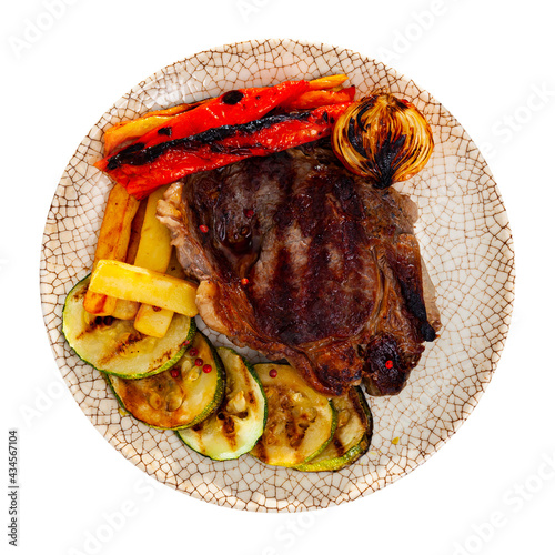 Plate with a delicious grilled beef steak with potatoes and appetizing bell peppers, a head of baked onions and sliced zucchini. Isolated over white background photo