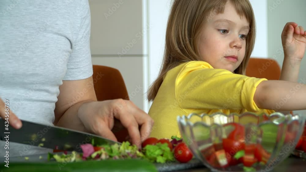 Little daughter helps father to prepare salad of fresh vegetables on kitchen. Happy child girl cook food of lettuce leaves and tomatoes. Little daughter helps father to prepare salad of fresh vegetables on kitchen. Happy child girl cook food of lettuce leaves and tomatoes.
