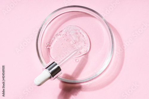 Pipette with a smear of hyaluronic acid on a round glass support, pink background. Cosmetics concept. photo