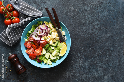 Mix salad with vegetables, leaves and feta. Greek salad in a plate on a blue concrete background. View from above.