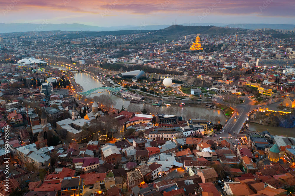 Scenic aerial view of historical area of Tbilisi on banks of Kura river and surroundings in evening lights in spring, Georgia
