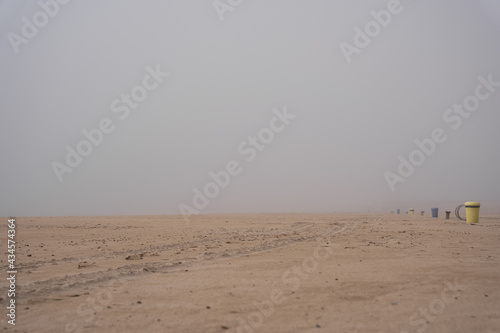 Baltic Sea beach in Ventspils covered with thick fog, garbage cans and benches in the distance