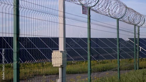 Solar Panels Fenced with Barbed Wire Fence. Solar batteries located on green grass by road, in a protected area behind a wire fence. Electricity generation. Restricted area. Lattice. 4K. Slow motion.