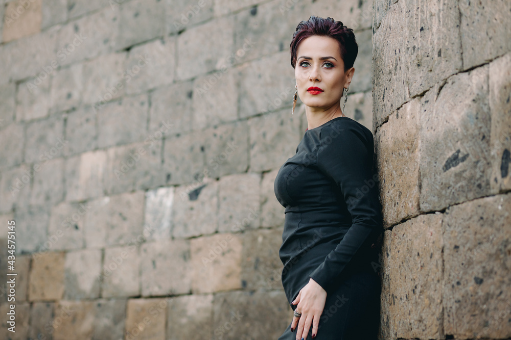Stylish and nice looking woman with black dress leaning on ancient castle and posing for camera. Stylish and nice looking woman with black dress leaning on ancient castle and posing for camera.