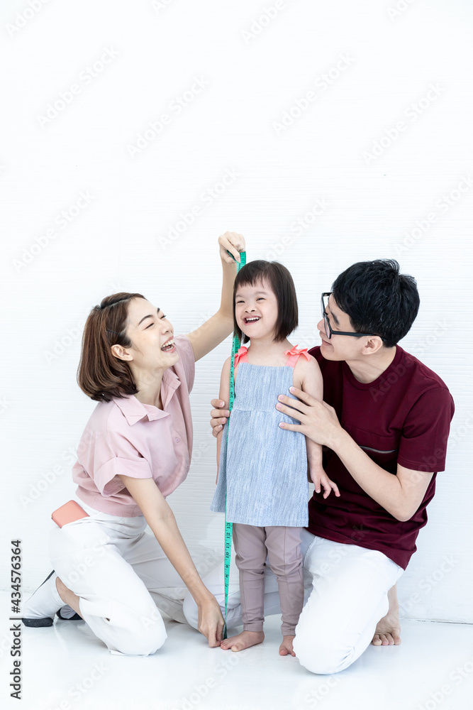 Father and mother, children, girls, disabilities, and cerebral development down syndrome are measuring daughter's waist circumference with a tape measure in the living room in the home. Father and mother, children, girls, disabilities, and cerebral development down syndrome are measuring daughter's waist circumference with a tape measure in the living room in the home.