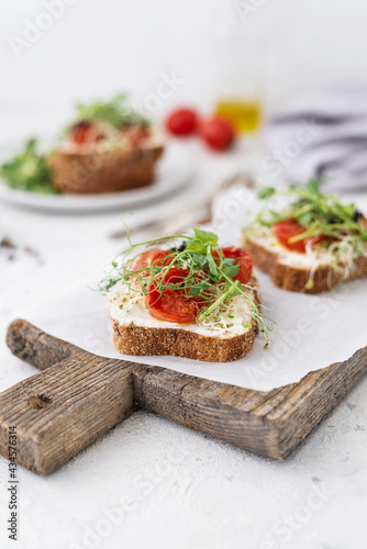 Healthy sandwich with cream cheese, baked tomatoes and micro greens on white background. Healthy breakfast sandwiches on a wooden board