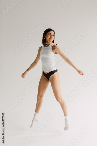 Εκτύπωση καμβά Fit young woman in white top, socks and black panties levitating on grey backgro