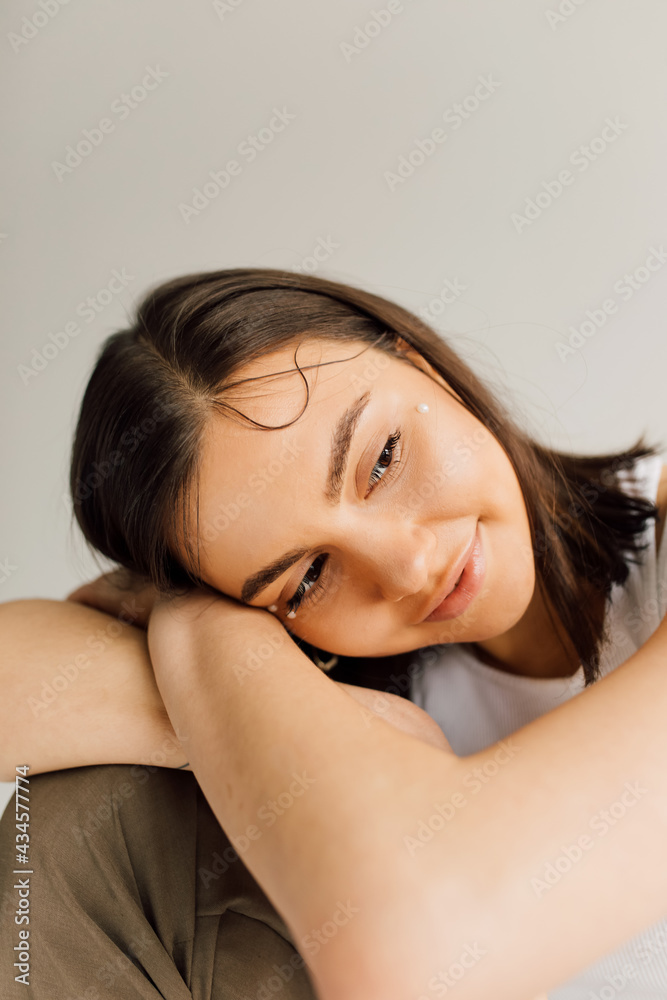thoughtful young woman with perfect skin sitting with head putted on crossed arms on grey background thoughtful young woman with perfect skin sitting with head putted on crossed arms on grey background