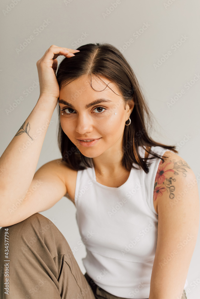 smiling young woman sitting with hand near face and looking at camera on gray background smiling young woman sitting with hand near face and looking at camera on gray background