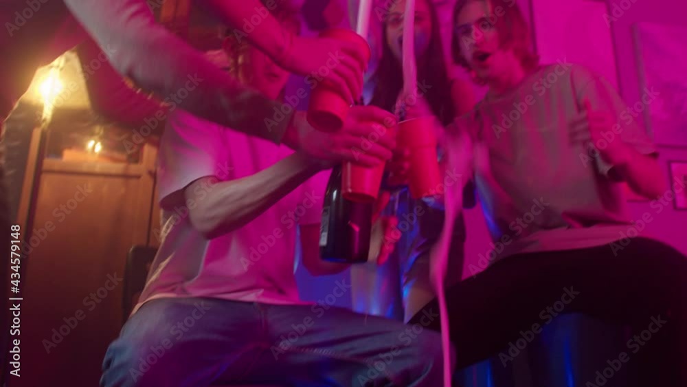 Teenagers friends celebrating happy birthday or Christmas at home during covid lockdown coronavirus party, young man pouring champagne, students drinking and dancing, having fun.