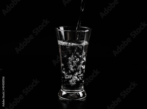 Pouring water into the glass on a black background.