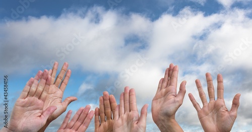 Composition of hands held up against clouds on blue sky