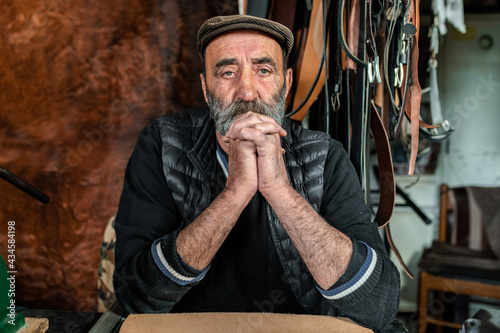 Portrait of old bearded hipster man looking at the camera. Craftsman working with genuine leather. © Pintau Studio