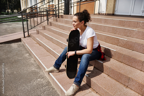 Beautiful young african american woman with skateboard sitting on steps of unrecognizable building