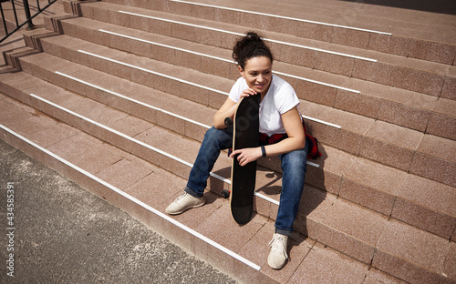 High angle view of a happy smiling woman with skateboard sitting on steps outdoors © Taras Grebinets