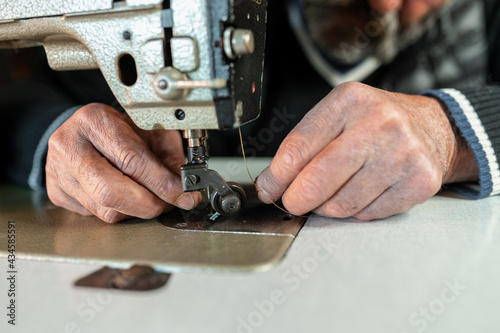 Close-up old male hands setting a sewing machine. Craftsmanship.
