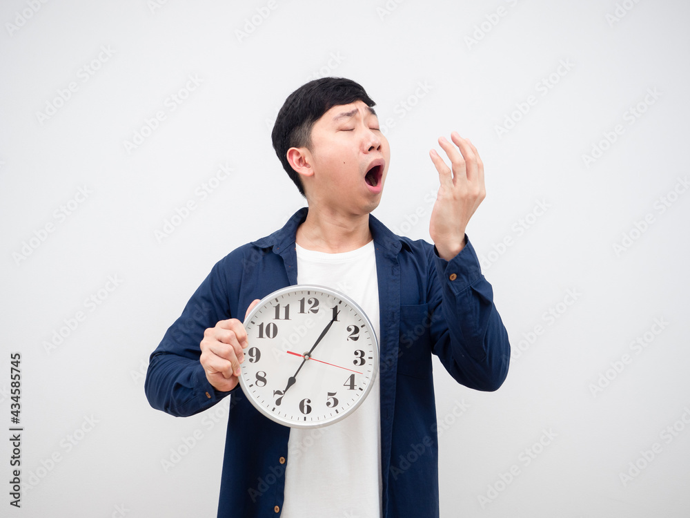Asian man feeling sleepy yawn holding clock in his hand on white background